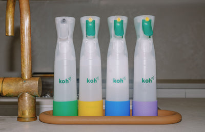 Koh Bottle Bumpers in green, yellow, blue, and purple fitted to four spray bottles on a kitchen counter